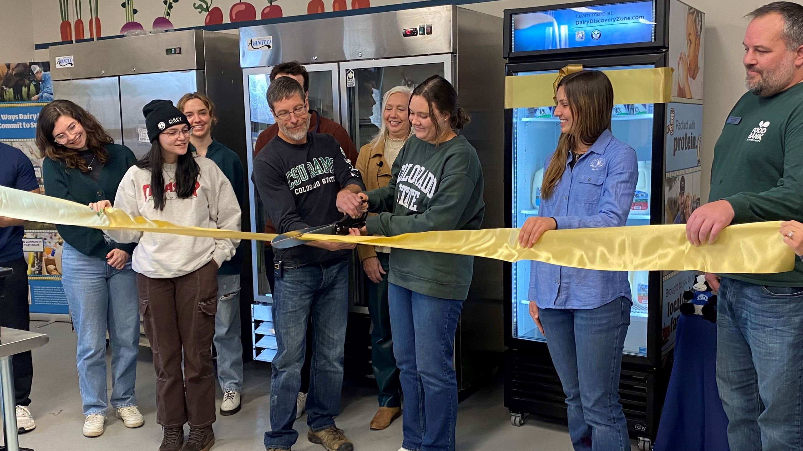Rams Against Hunger employees and student volunteers cut a ribbon to celebrate the donation of a Dairy MAX dairy cooler in the food pantry.