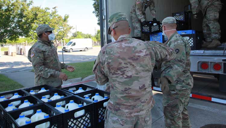 national guard members help load up gallons of milk on a truck