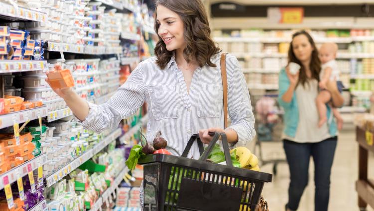 Woman grocery shopping holding a basket in an isle.