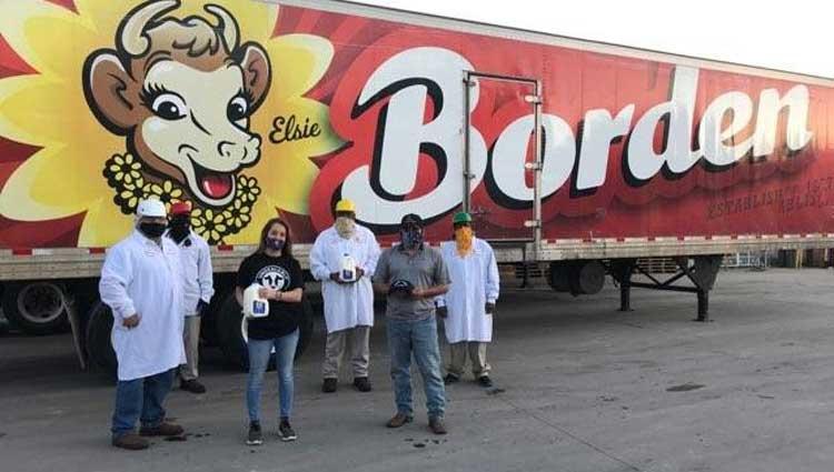 people in protective gear holding gallons of milk in front of a Borden trailer