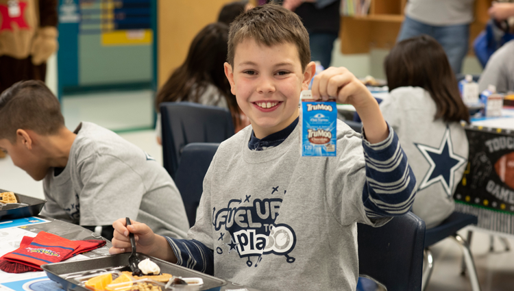 young boy drinks chocolate milk with his school breakfast in a fuel up to play 60 t shirt